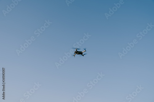 Grey little drone flies in the blue sky.