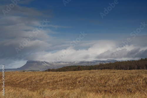 View on a field in county Sligo, Ireland. famous Benbulben flat top mountain in the background, Top covered with clouds and snow, warm sunny day, Cloudy sky, Nobody,