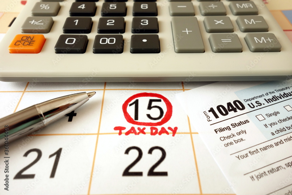 Monthly calendar showing date July 15th 2020 marked as tax day with 1040 form calculator and pen Monthly calendar showing date July 15th 2020 marked as tax day with 1040 form calculator and pen