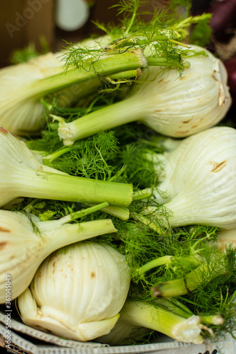Fresh garlic with dill is sold in a large white basket at the market or in the store outside.