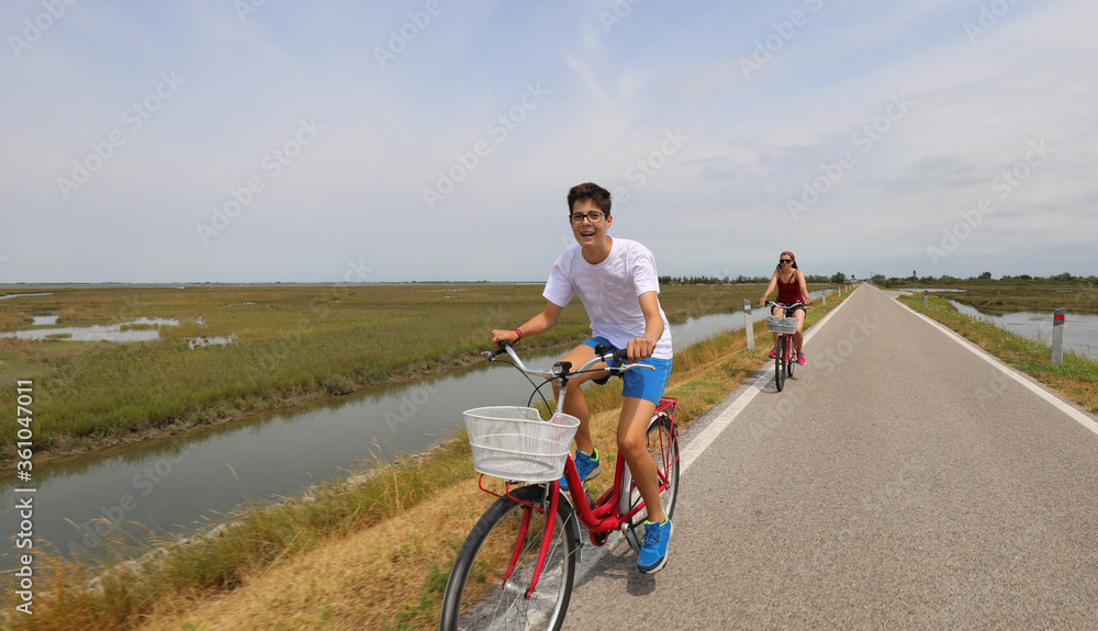 cheerful boy pedaling bicycle on bicycle path with his mom