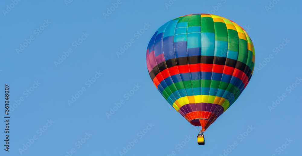 Naklejka premium Balloon flying high in the sky. Balloon basket with people. Aeronautic sport. Burning gas. Bright multi-colored balloon. Romantic trip. Free space for text.