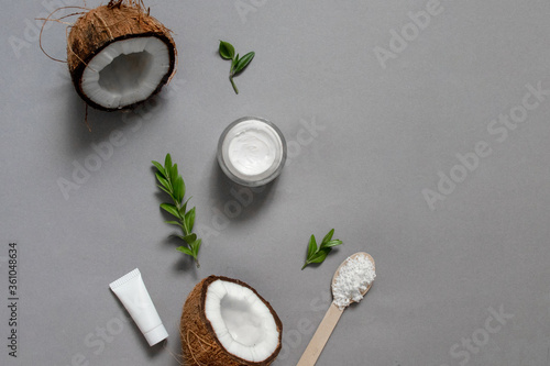 Homemade coconut oil cosmetics for skin and hair care. Oil in small bottle, face cream, halves of coconut with shelf on grey background, top view copy space