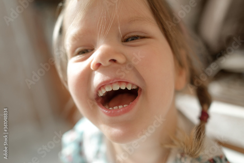 A cheerful five-year-old girl laughs hard close to the camera in soft focus. She has bright eyes, baby teeth, and pigtails. Child is surprised react to the gift.