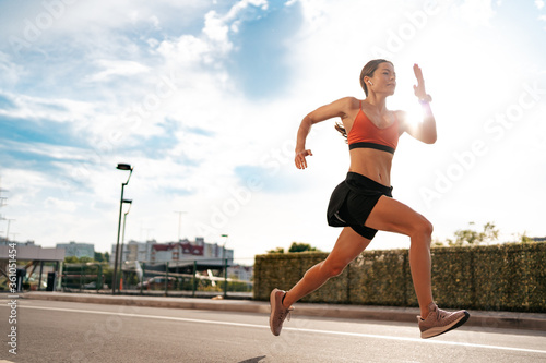 Young woman sprinting in the morning outdoors. Side view of female runner working out in the city with sky in background