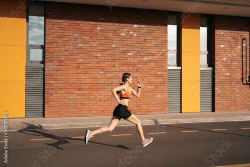 Young woman sprinting in the morning outdoors. Side view of female runner working out in the city.