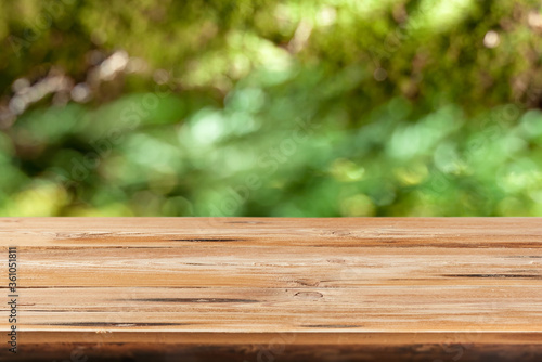 Aged wooden table for montage or display products on a green leaves blurred background.