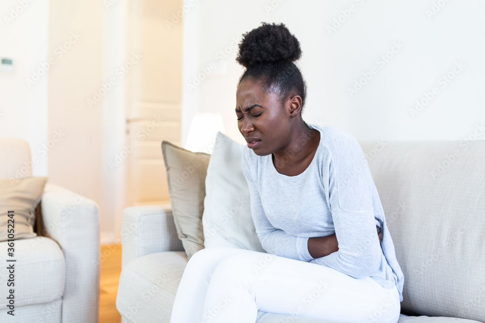 Woman in painful expression holding hands against belly suffering menstrual period pain, lying sad on home bed, having tummy cramp in female health concept Woman in painful expression holding hands against belly suffering menstrual period pain, lying sad on home bed, having tummy cramp in female health concept
