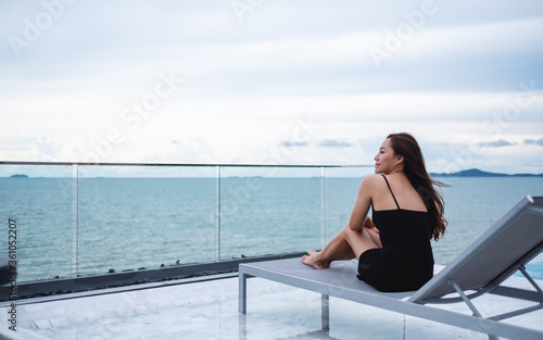 A beautiful young asian woman sitting next to the rooftop pool , looking at the sea and blue sky view © Farknot Architect
