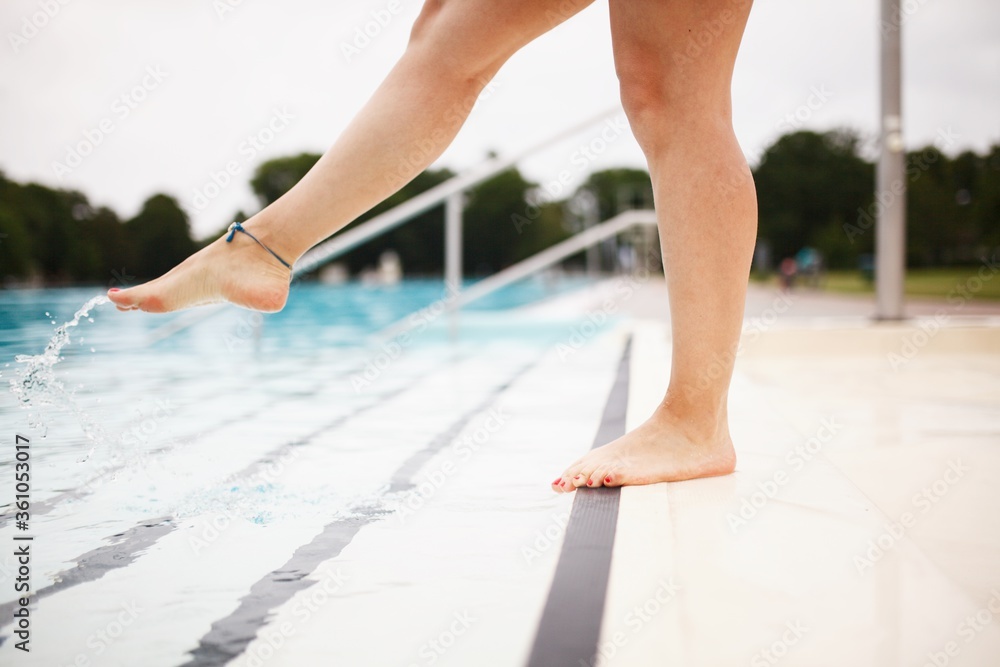 Young adult woman's  feet by the pool, checking the water temperature,  making splashes.