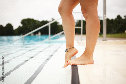 Young adult woman's feet by the pool, checking the water temperature. 