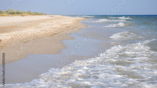 Beautiful seascape with foam sea waves, deep blue water and golden sand shore.