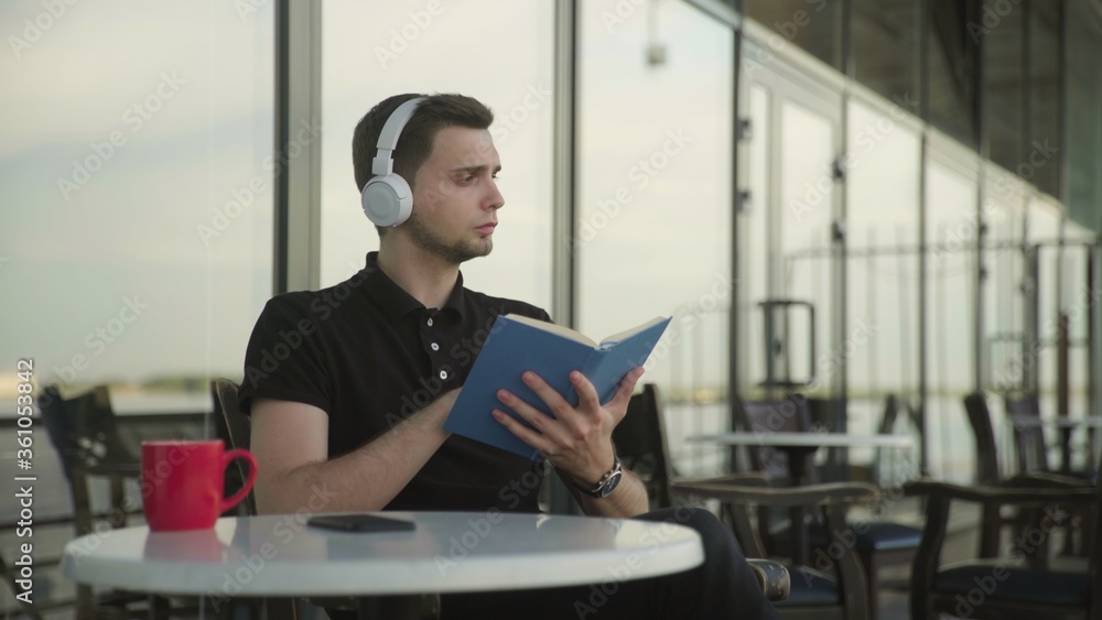 Young handsome man sitting in park cafe reading a book Young handsome man sitting in park cafe reading a book