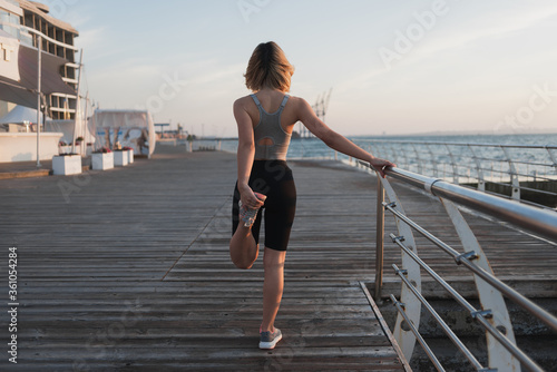 young woman athlete doing warm-up early in the morning. Fresh air. Pier near the ocean. Copy space.