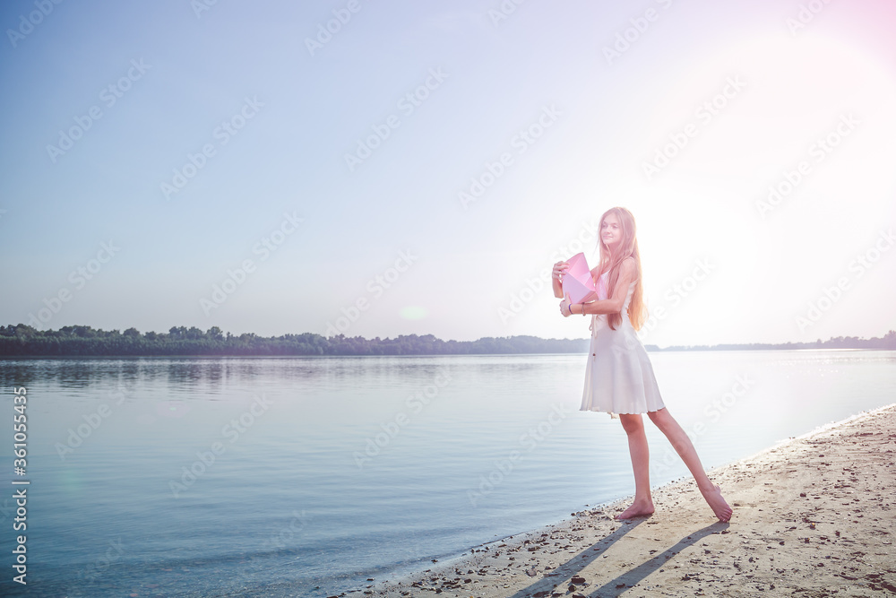Teenager girl with long hair in white dress holding a big pink paper ...