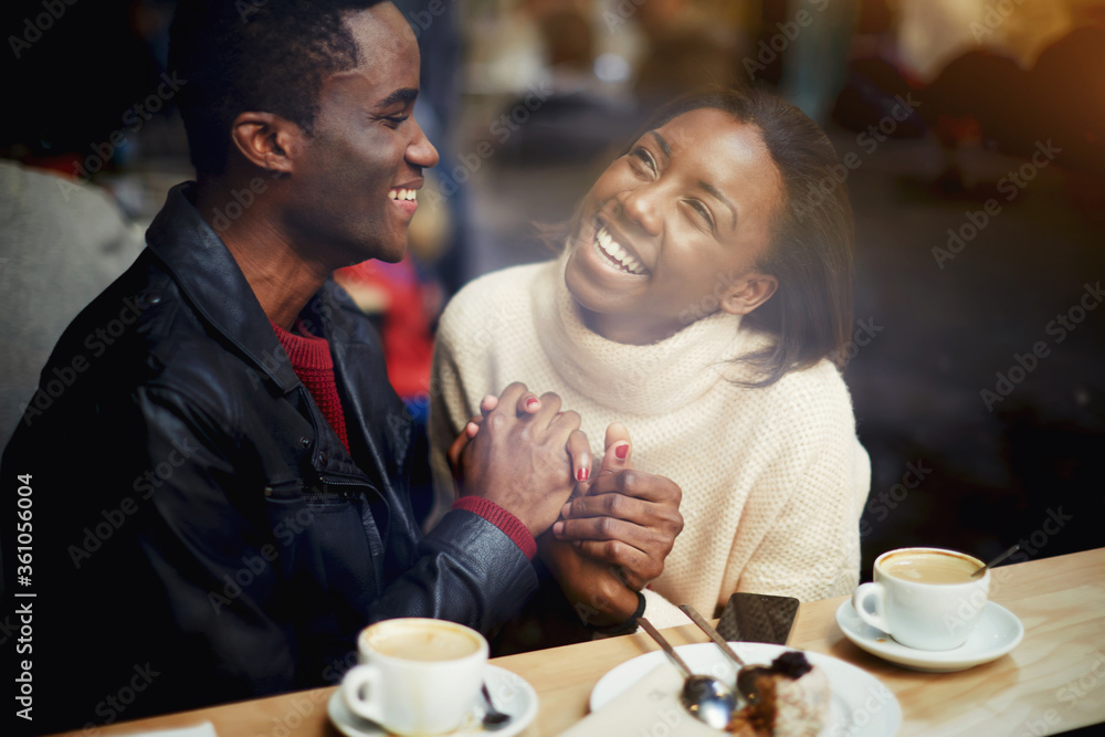 View through window of cheerful happy lovers enjoying leisure while sitting in bar in cold winter day, young black man and woman with beautiful smiles on faces having fun during rest in coffee shop View through window of cheerful happy lovers enjoying leisure while sitting in bar in cold winter day, young black man and woman with beautiful smiles on faces having fun during rest in coffee shop