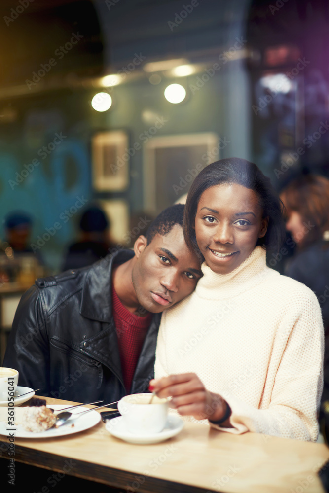 View through window of a charming young woman sitting in cafe with her boyfriend,  dark skinned couple enjoying themselves and good day while relaxing in bar, lovers posing during coffee break