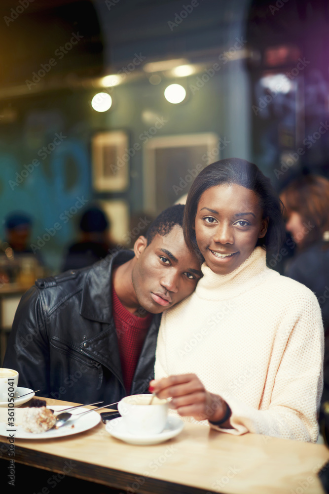 View through window of a charming young woman sitting in cafe with her boyfriend, dark skinned couple enjoying themselves and good day while relaxing in bar, lovers posing during coffee break View through window of a charming young woman sitting in cafe with her boyfriend, dark skinned couple enjoying themselves and good day while relaxing in bar, lovers posing during coffee break