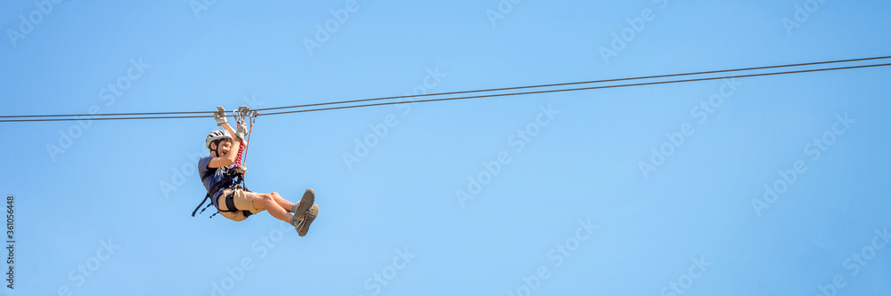 Teenager having fun in summer on a zipline on panoramic blue sky background with copy space