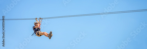 Teenager having fun on a zipline on panoramic blue sky background with copy space. photo