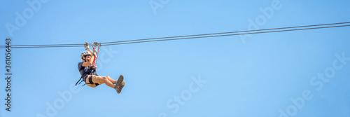 Obraz na płótnie Teenager having fun in summer on a zipline on panoramic blue sky background with copy space w salonie