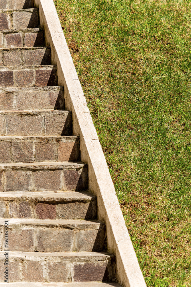 Closeup of a staircase made of porphyry stones with a green lawn next to it. Italy, Europe