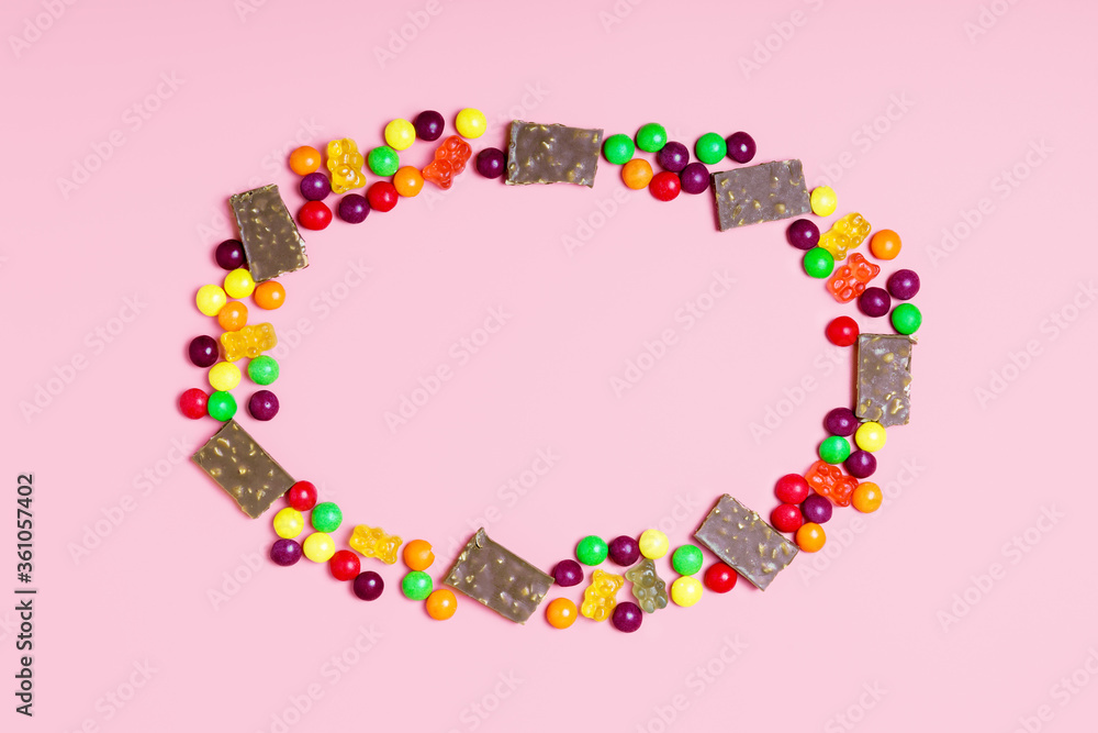 Frame of pieces of chocolate, jelly bears and round candies on a pink background. sweets concept for kids. border, top view, copy space.