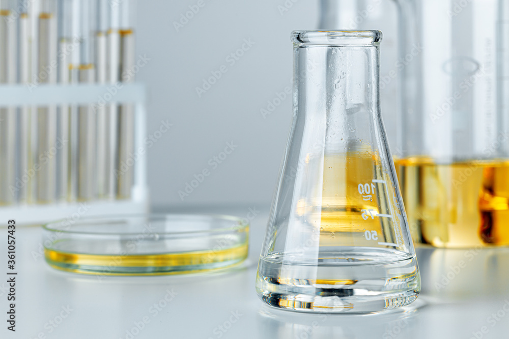 Laboratory glassware with yellow oily liquid on grey background Laboratory glassware with yellow oily liquid on grey background