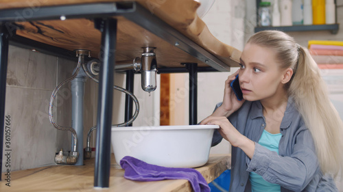фотографія Woman sitting near leaking sink in laundry room calling for help