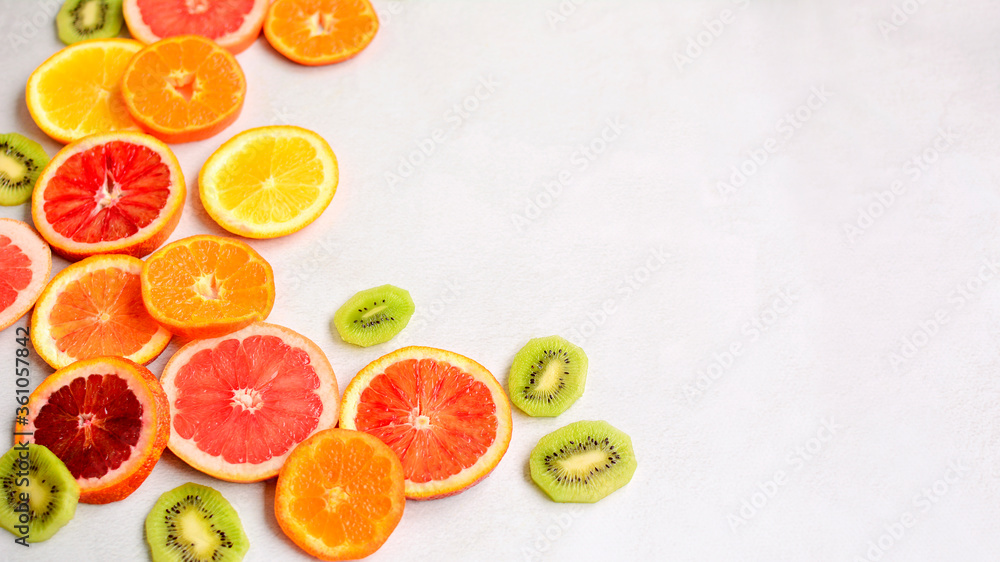 Close-up of sliced red orange, tangerines, green kiwi and grapefruit on a light gray background. Side space for lettering and design. Close-up of sliced red orange, tangerines, green kiwi and grapefruit on a light gray background. Side space for lettering and design.