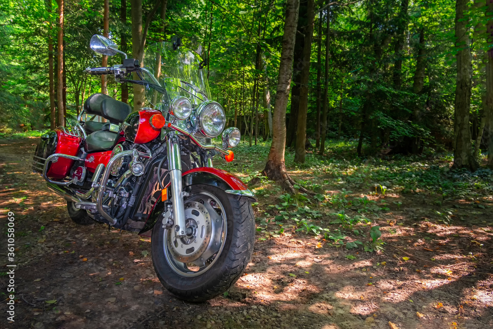 Motorcycle cruiser stands on dirt road in sunny green forest. Walk ride on chopper in forest road Motorcycle cruiser stands on dirt road in sunny green forest. Walk ride on chopper in forest road