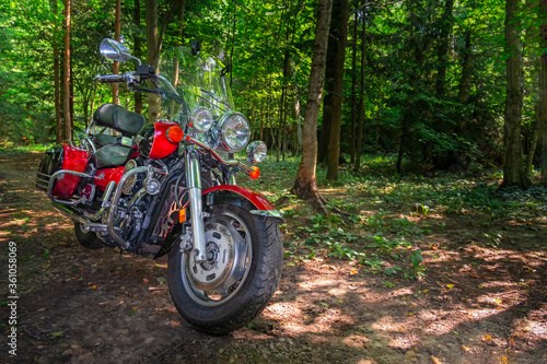 Motorcycle cruiser stands on dirt road in sunny green forest. Walk ride on chopper in forest road