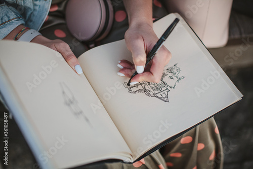 Sketchbook with a drawing of a house close-up. Girl draws with her left hand.