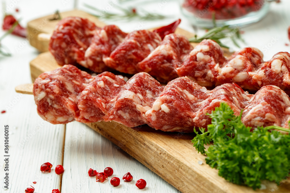 Raw lula kebab on skewers with spices on wooden board Raw lula kebab on skewers with spices on wooden board