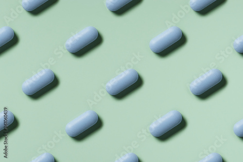 medicine, healthcare and pharmacy concept - blue pills or capsules lie in rows diagonal on mint green background top view copy space pattern