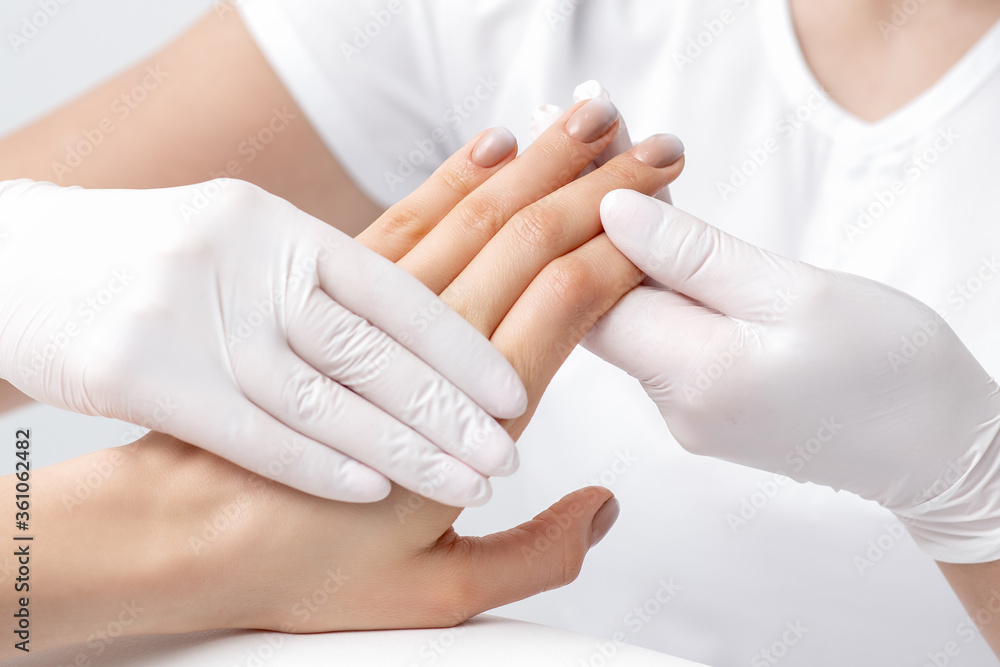 Human hands in protective gloves holding female fingers with beige polish on nails in beauty salon Human hands in protective gloves holding female fingers with beige polish on nails in beauty salon