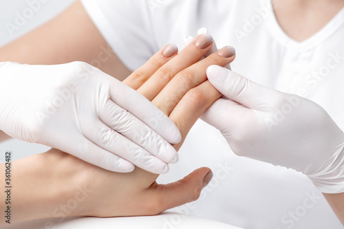 Human hands in protective gloves holding female fingers with beige polish on nails in beauty salon