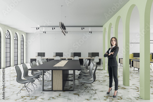 Attractive businesswoman standing in coworking office interior with meeting table