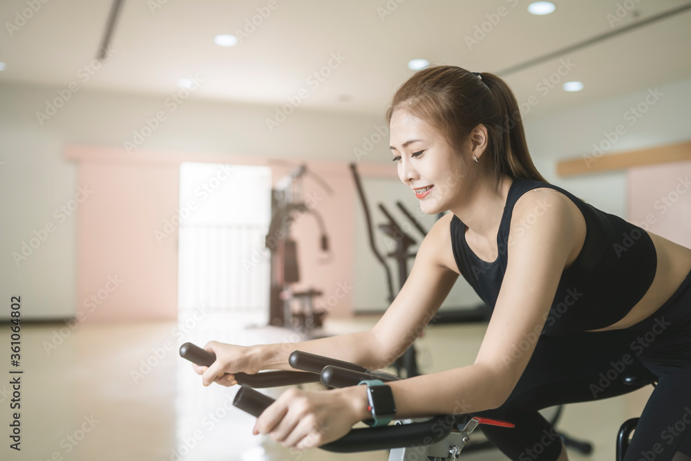 Beautiful Asian woman riding and exercising on the spinning bike at the fitness gym.