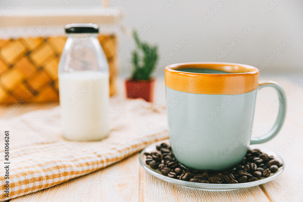 Cup of black coffee and coffee beans on saucer with bottle of milk on wooden table, breakfast Cup of black coffee and coffee beans on saucer with bottle of milk on wooden table, breakfast