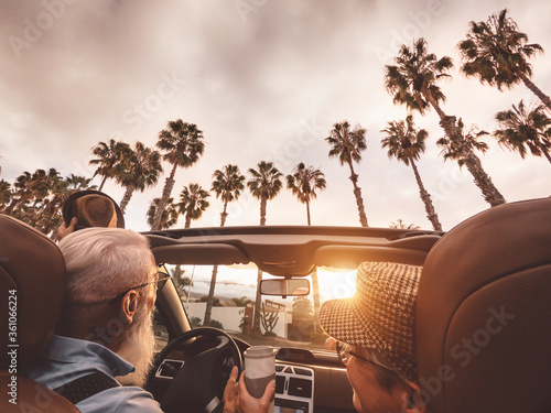 Happy senior couple having fun driving on new convertible car - Mature people enjoying time together during road trip tour vacation - Elderly lifestyle and travel culture transportation concept