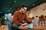 Cheerful man using laptop in a cozy restaurant, portrait.
