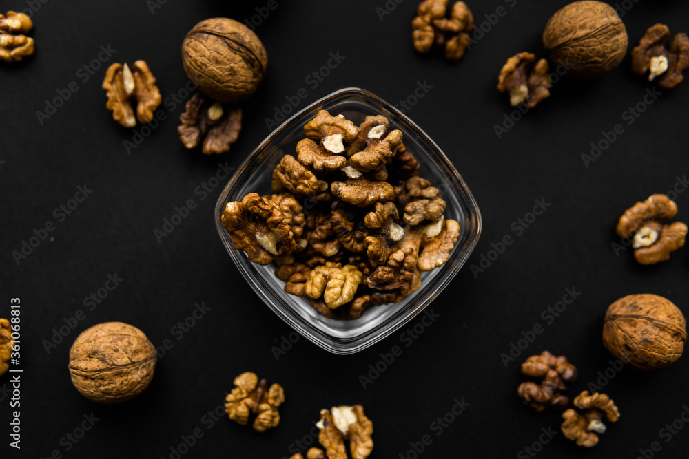 Walnut in a small plate with scattered shelled nuts which standing on a black surface. Walnuts is a healthy vegetarian protein nutritious food. Walnut in a small plate with scattered shelled nuts which standing on a black surface. Walnuts is a healthy vegetarian protein nutritious food.