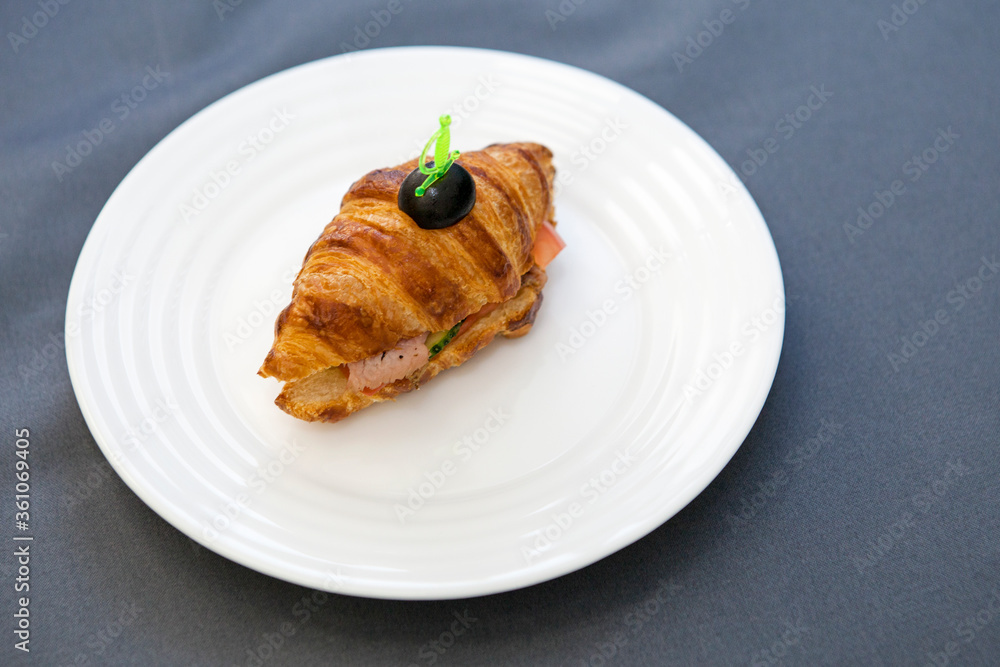 Croissant sandwich with turkey, cheese and vegetables. White plate, gray background, selective focus