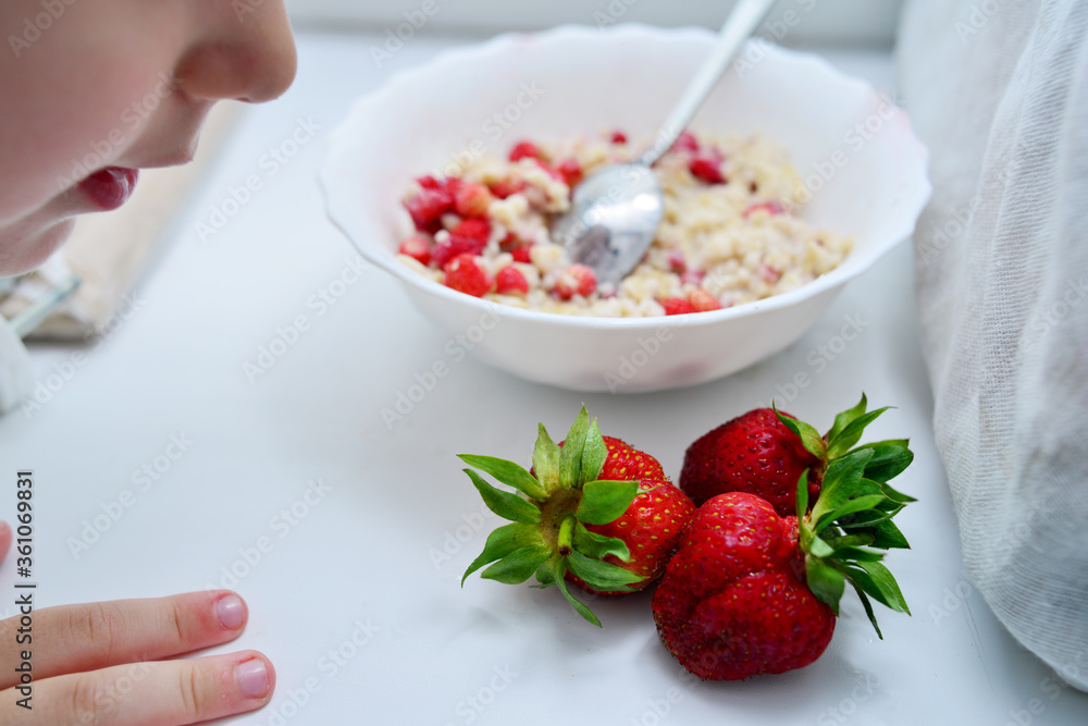 Red juicy strawberries with a plate of porridge on a light table. Healthy breakfast Red juicy strawberries with a plate of porridge on a light table. Healthy breakfast