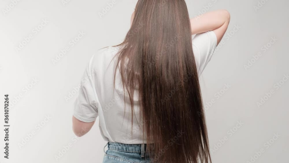 Close-up brunette developing hair in studio on a white background. Rear view of a girl with beautiful manicured hair. Close-up brunette developing hair in studio on a white background. Rear view of a girl with beautiful manicured hair.