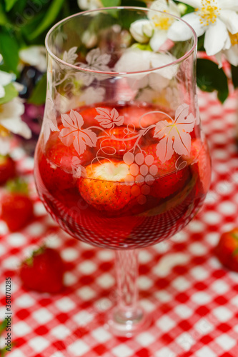 Glass of rose wine with fresh strawberries on Jasmine flowers, bottle of wine, strawberries, red checkered tablecloth, summer background