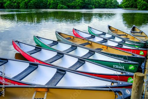 Colourful canoes and kayaks moored and tied to a wooden pontoon in Salhouse Broad in the Norfolk Broads