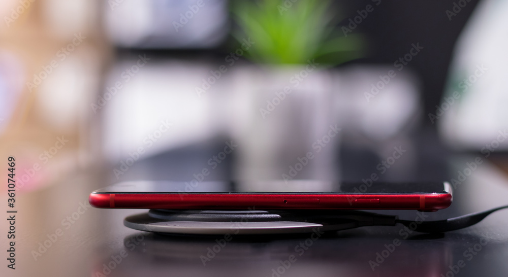 Phone charging on wireless charger. New technology. Red phone on charger board. Red phone on black desk.