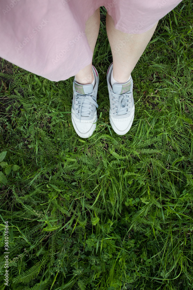 Top view of a girl in a dress and sneakers on the grass, vertical photo